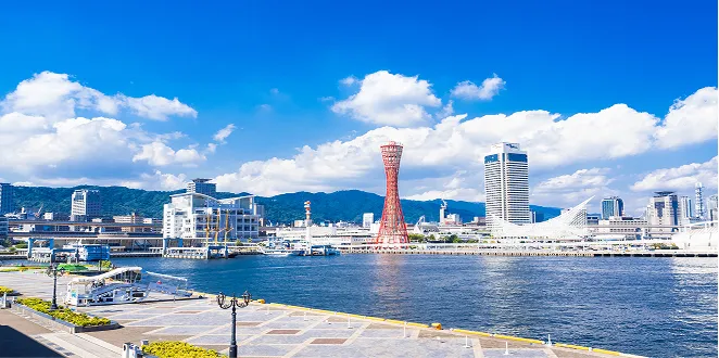神戸港に架かる赤いポートタワーと、青空の下に広がる港のベイエリアの景観。