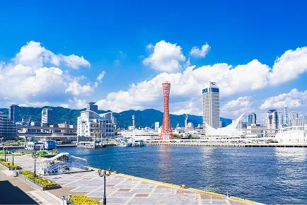港に面して立つ赤い鉄塔状の神戸ポートタワー。周辺には海沿いの施設や建物が広がる。