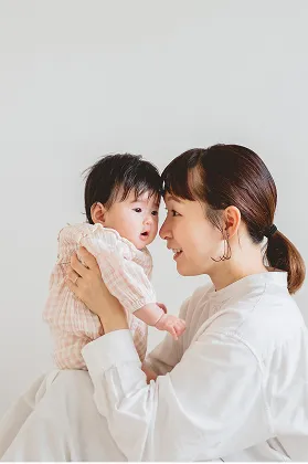 母親が赤ちゃんを優しく抱き上げ、額を寄せ合いながら微笑み合っている様子。