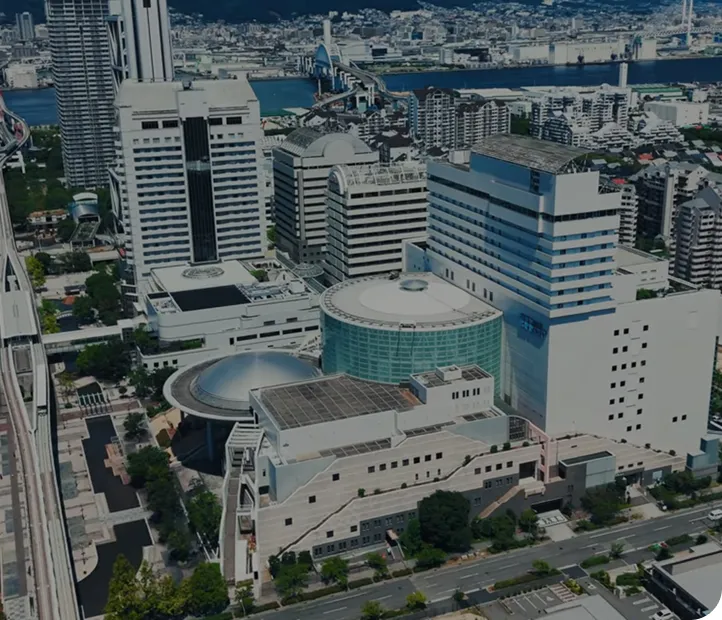神戸の街並みを上空から見下ろした風景。高層ビルが立ち並ぶ中、モノレールの高架線とドーム状の建物が並ぶ一角にホテルプラザ神戸が建っている。