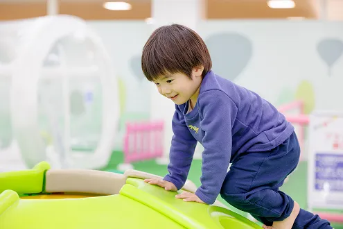室内遊び場で、黄緑色の滑り台に楽しそうによじ登る男の子。