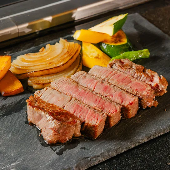 黒い鉄板の上に並べられた厚切りのステーキと、彩り豊かな焼き野菜。鉄板焼ならではの豪華な一皿。