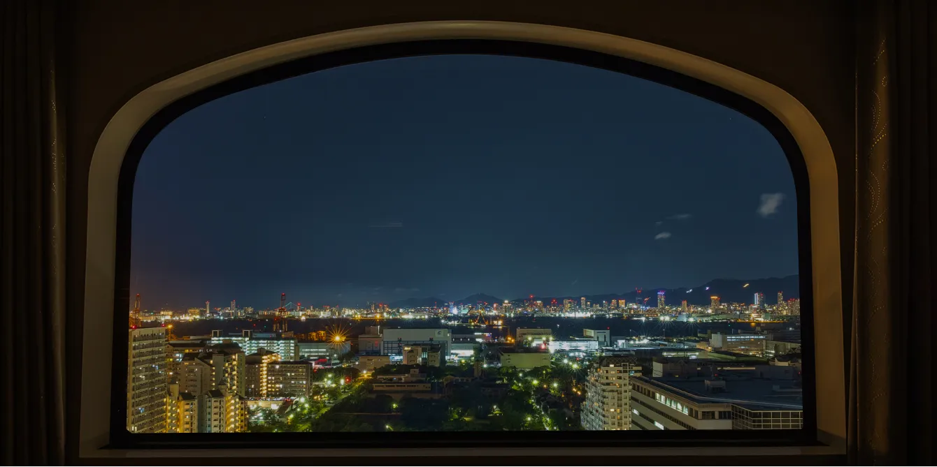 アーチ型の窓越しに広がる神戸港の夜景。暗い夜空の下、無数の明かりが灯る建物群と港の施設が幻想的な景色を作り出している。