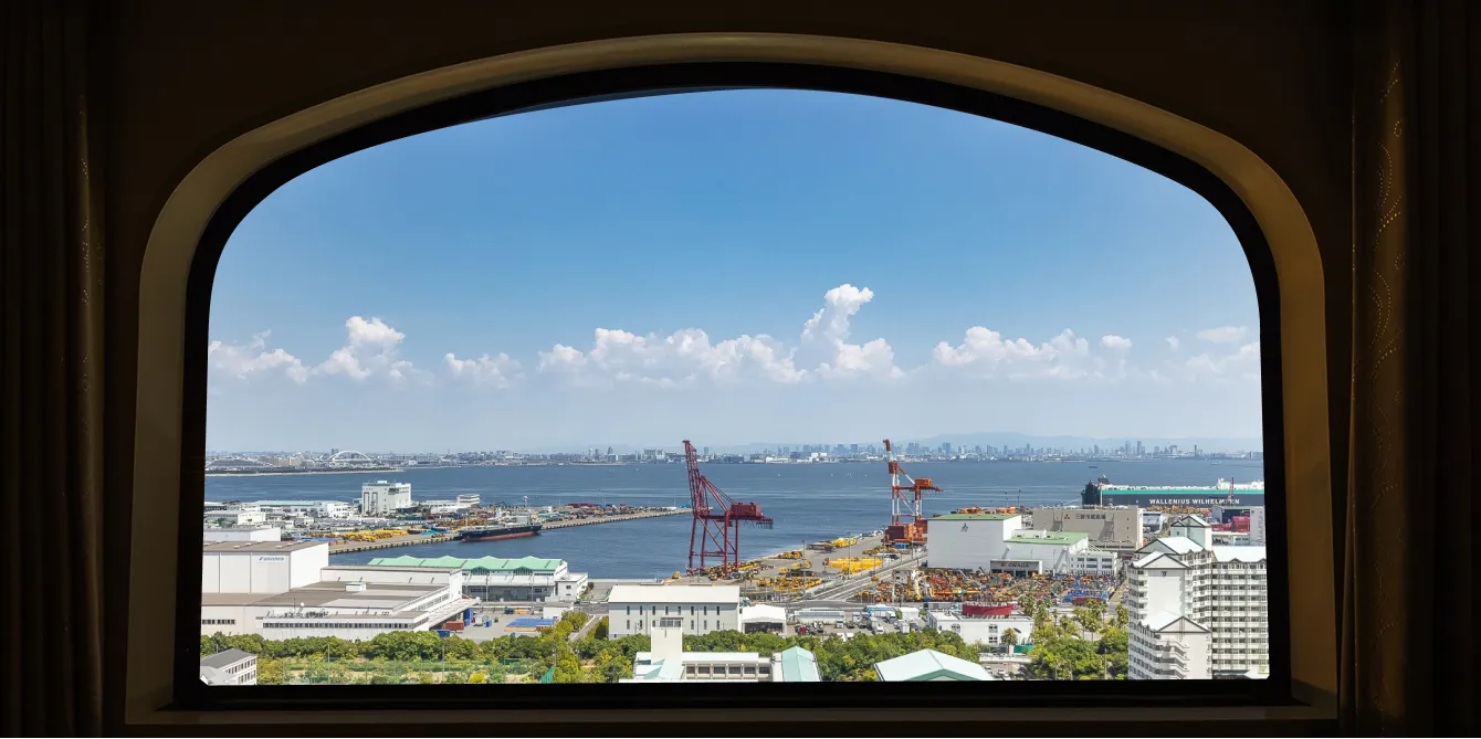 アーチ型の窓越しに広がる大阪湾方面の景色。青空に雲が浮かび、港のクレーンや対岸の高層ビル群までが見渡せる。