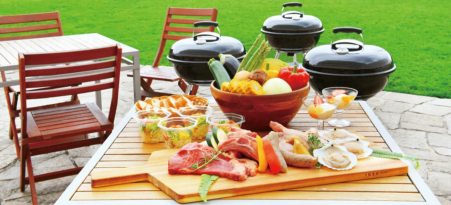 緑の芝生を背景に、屋外テーブルに用意された肉や野菜のBBQ食材