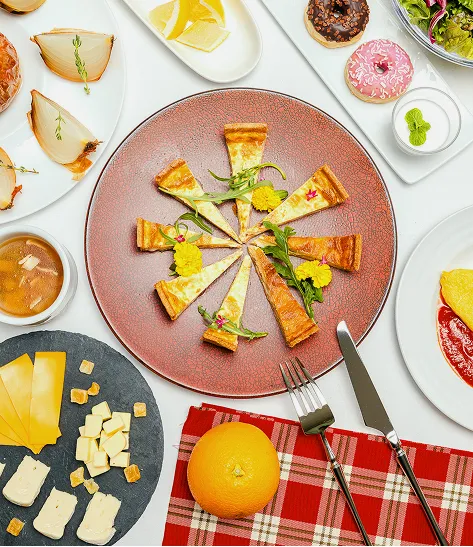 花で彩られたクレープ料理を中心に、ドーナツやサラダ、チーズプレートなど色とりどりの料理が並ぶ朝食の一例。