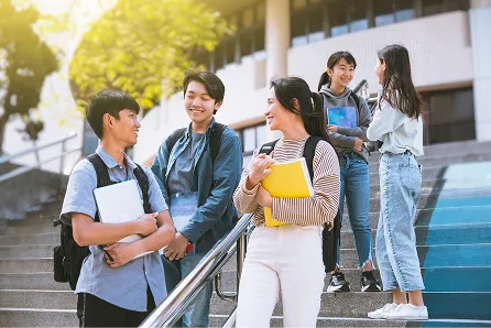 階段の上で談笑する学生グループ。リュックや荷物を持った男女が数名集まっている。