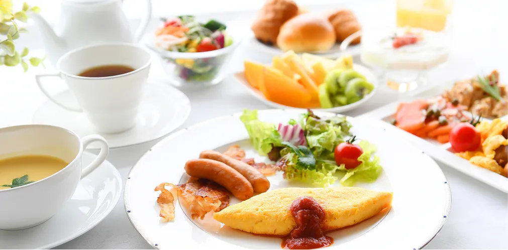 オムレツ、ソーセージ、サラダ、フルーツ、スープが並ぶ洋食朝食膳