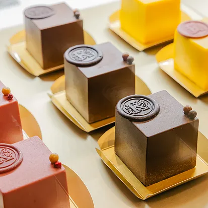 チョコレートやオレンジ、いちご風味の正方形のケーキに刻印入りの蜜蝋のシールが飾られ、金色の台紙に並べられている。