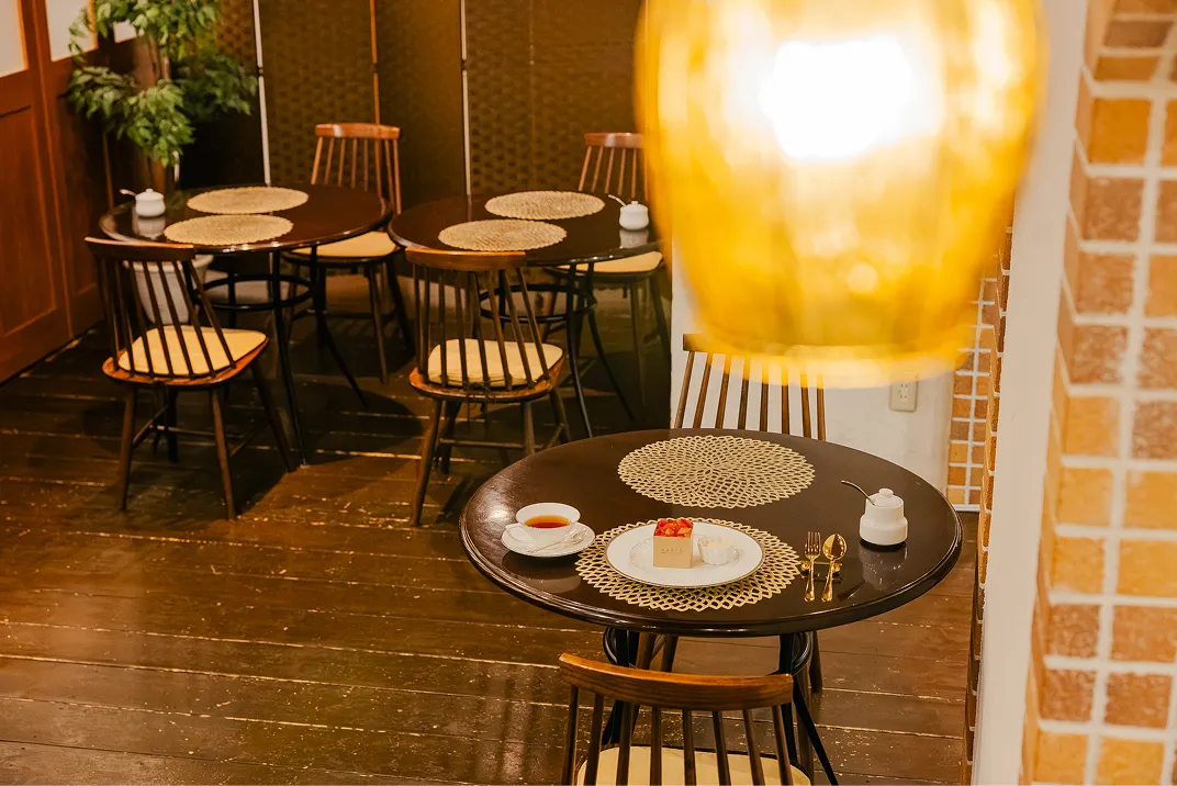 木目の天井と大きな窓のある明るい店内に丸テーブルと木製の椅子が並び、奥にはレンガ造りのアーチ型の壁が見える落ち着いた雰囲気の客席。