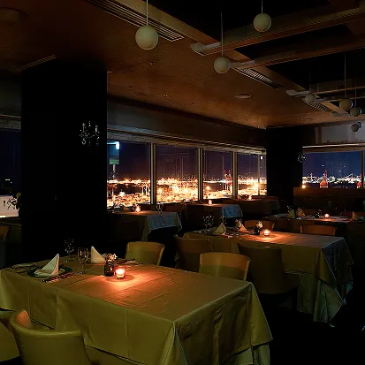 夜の店内に暖かみのあるキャンドルの明かりが灯り、窓の外には港町の夜景が一面に広がっている。