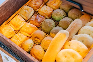 木箱に、丸いねじりパンや抹茶色の丸パン、細長いバゲットなど数種類の焼きたてパンが並ぶ様子。