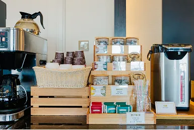 コーヒーメーカーとポットの横に、紙コップや数種類の茶葉パックを木箱に並べたドリンクコーナー。