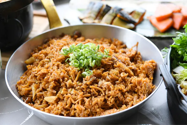甘辛く炒めた具材に刻んだ青ねぎを散らした炒めご飯を鍋いっぱいに盛り付け、脇に焼き魚を添えた様子。