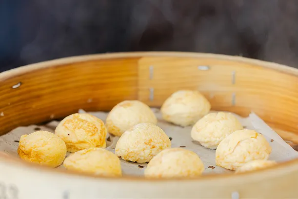 蒸し器の中に、ふっくらと膨らんだ丸い明石焼きが並び、湯気が立ちのぼっている様子。