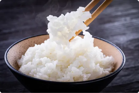 黒い茶碗に盛った白いご飯を、湯気の立つ状態で箸で持ち上げている様子。