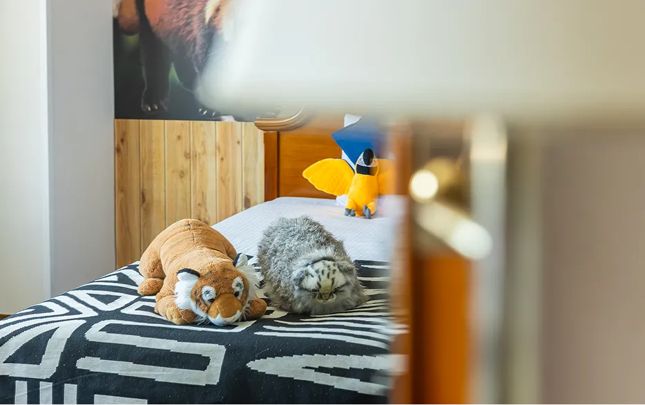 トラやユキヒョウのぬいぐるみが置かれたベッドと、背景にレッサーパンダが描かれた壁画。