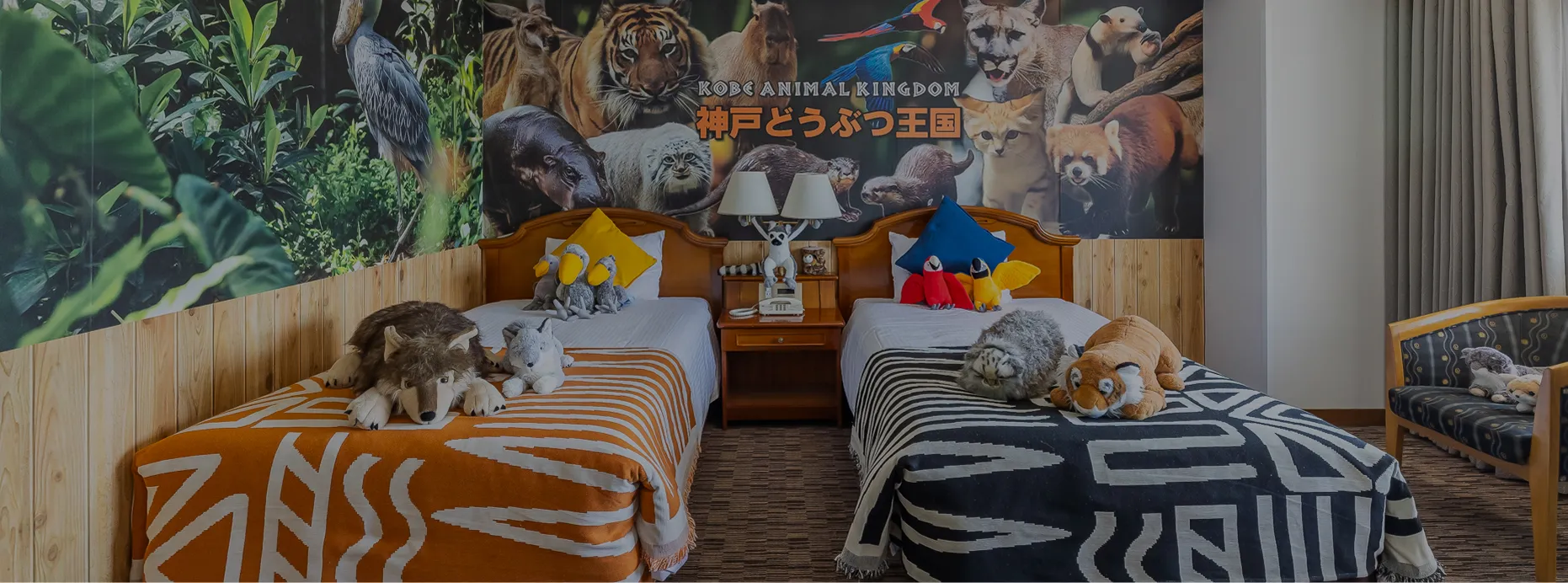 神戸どうぶつ王国の動物たちが描かれた壁一面のウォールアートが印象的なツインルーム。ベッドには動物のぬいぐるみが飾られている。