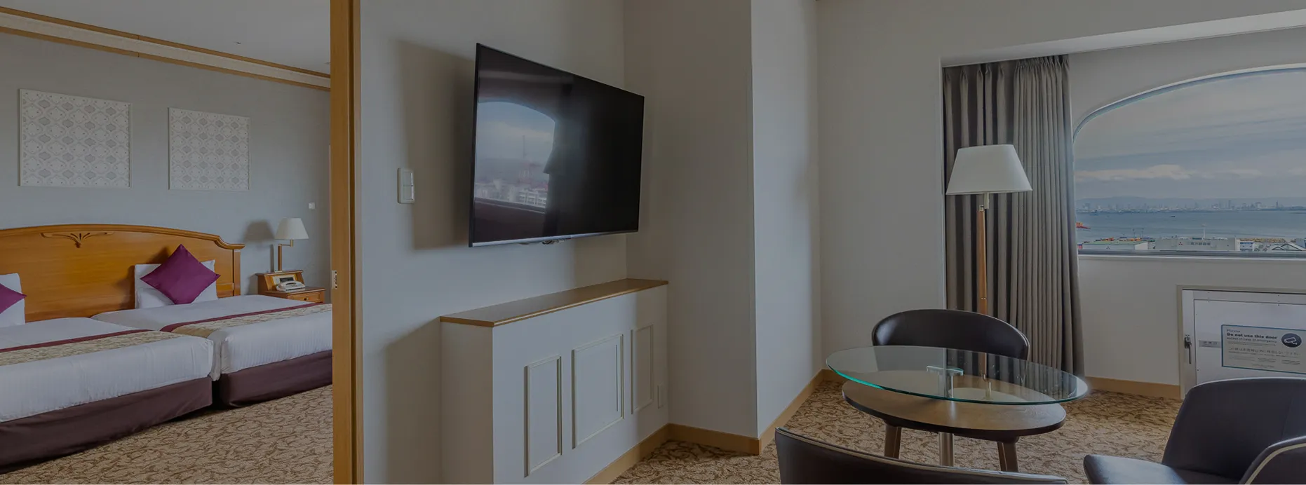 扉でつながる2つの空間からなるファミリースイートルーム。手前にはテレビとテーブル、海を望む窓のあるリビングスペースが広がる。