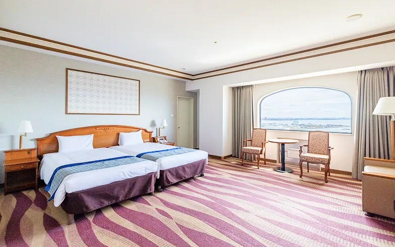 アーチ窓から海を望む、角部屋タイプのコーナーツインルーム。2台のベッドの奥に、くつろげる椅子とテーブルのスペースが広がる。