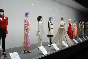 ガラスケースの中に色とりどりの衣装を着たマネキンが一列に並ぶ、神戸ファッション美術館の展示風景