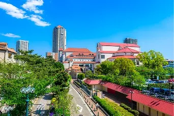 青空の下、緑の並木道の先に赤い屋根の洋風建築やタワーマンションが並ぶ宝塚の街並み