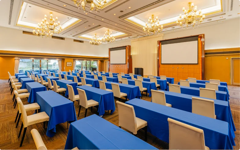 白いチェアカバーと紺色のテーブルクロスで整えられた円卓が並ぶ昼の会場。開け放たれた両側の掃き出し窓から、芝生の庭園が見渡せる。