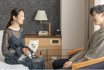 子犬を膝に乗せ座っている女性と椅子に座っている男性が笑顔で楽しそうに会話している様子