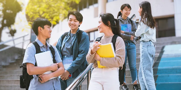 学生服やカジュアルな私服姿の学生グループが、笑顔で会話しながら屋外の階段を歩いている様子。
