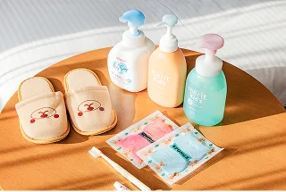 くまの刺繍が入った子供用スリッパと、シャンプーなどのボトル、おしぼりが円形のテーブルに並べられている。